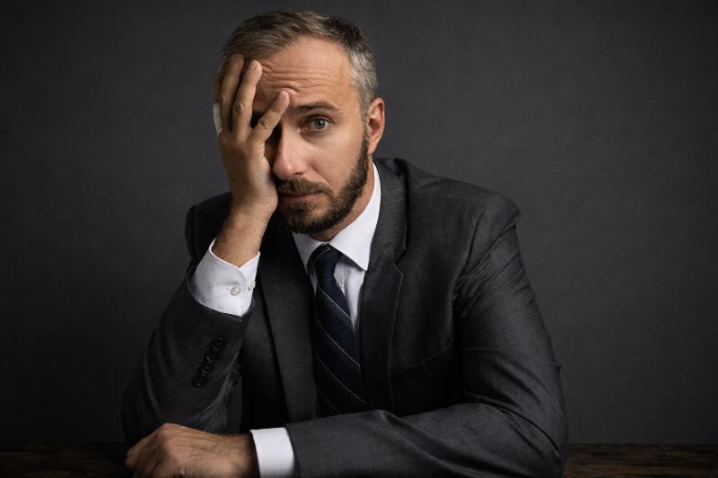 Jan Böhmermann sitzt im Anzug an einem Tisch, hält die Hand an die Stirn und blickt nachdenklich in die Kamera.