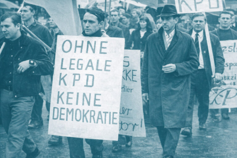Demonstration gegen das KPD-Verbot 1956: Mehrere Männer marschieren mit Transparenten, im Vordergrund ein Schild mit der Aufschrift „Ohne legale KPD keine Demokratie“.