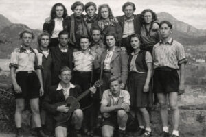 Historische Schwarzweißaufnahme einer Gruppe junger Edelweißpiraten, die 1943 gemeinsam im Freien vor dem Drachenfels mit Gitarre posieren.