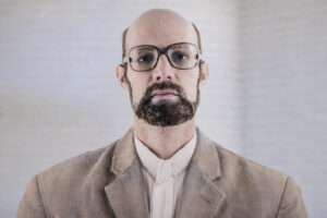 Josef Kneifel (1980) mit mit Brille und Bart, frontal aufgenommen, neutraler heller Hintergrund