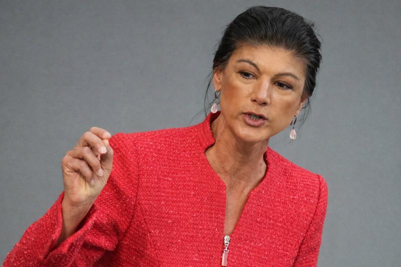 Sahra Wagenknecht spricht und gestikuliert in roter Jacke vor neutralem Hintergrund