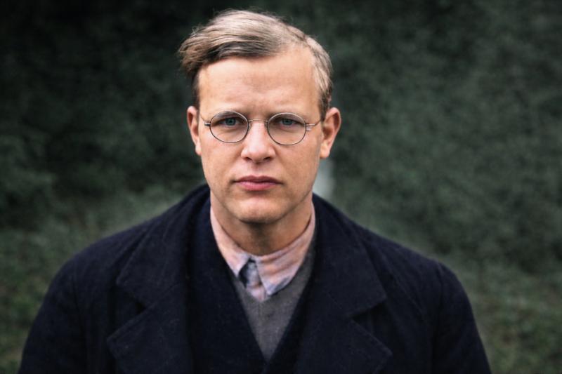 Porträt von Dietrich Bonhoeffer, deutschem Theologen und Widerstandskämpfer gegen den Nationalsozialismus, mit runder Brille vor unscharfem grünem Hintergrund