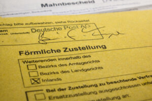 Nahaufnahme eines gelben Mahn- und Zustellungsformulars mit dem Text "Förmliche Zustellung" und angekreuztem Kästchen „Inlands“
