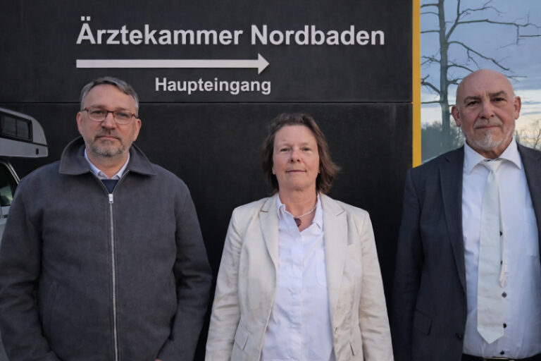 Monika Jiang mit ihren beiden Anwälten vor einem Gebäude mit der Aufschrift „Ärztekammer Nordbaden“ und dem Hinweis „Haupteingang“ mit Pfeil nach rechts.