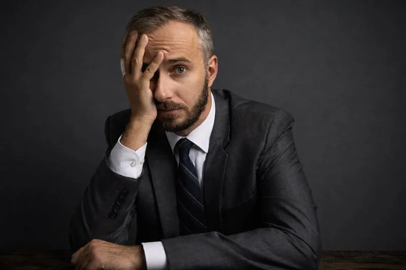 Doxing durch den ÖRR: Jan Böhmermann „doxt“ Marc-Philipp Längert (Clownie) 1 Jan Böhmermann sitzt im Anzug an einem Tisch, hält die Hand an die Stirn und blickt nachdenklich in die Kamera.