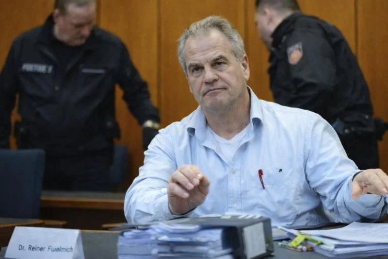 Political Prisoners: The Case of Reiner Fuellmich - Kennedy Associate Lehrman Raises Heavy Accusations Against German Judiciary 1 Reiner Füllmich sitzt im Gerichtssaal an einem Tisch mit Akten, im Hintergrund stehen zwei Polizeibeamte.