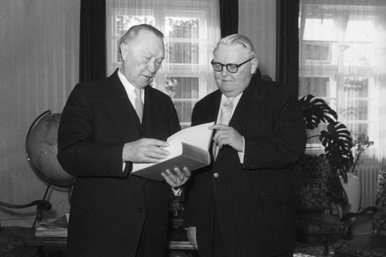 Konrad Adenauer: Vom Kölner Oberbürgermeister zum Staatsfeind des NS-Regimes – Eine Chronik der Verfolgung 1 Bundeskanzler Konrad Adenauer liest interessiert in dem Buch, das ihm Bundes-Wirtschaftsminister Prof. Erhard als Geburtstagsgeschenk überreichte (1956)