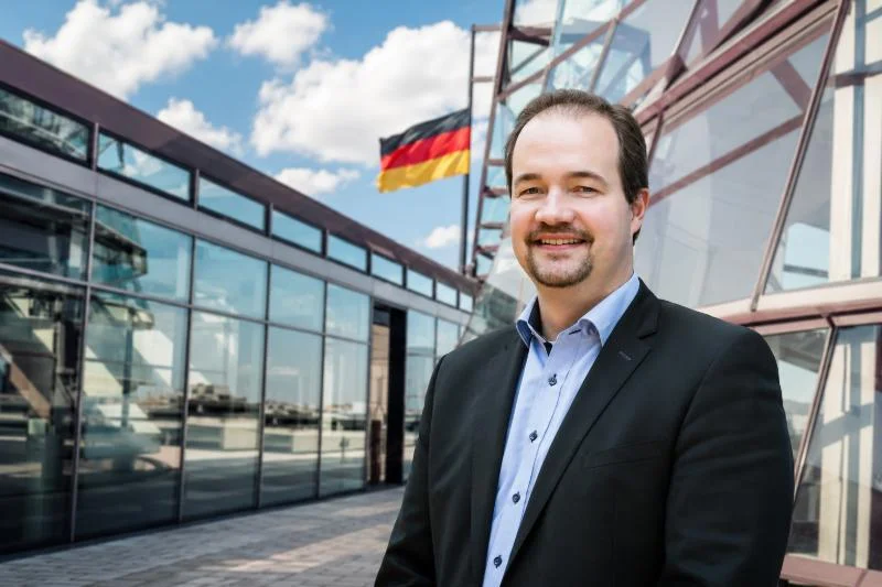 Martin Sichert vor einem Regierungsgebäude mit Deutschlandfahne